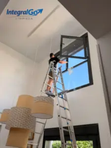 Operario limpiando por dentro una ventana en altura subido a una escalera